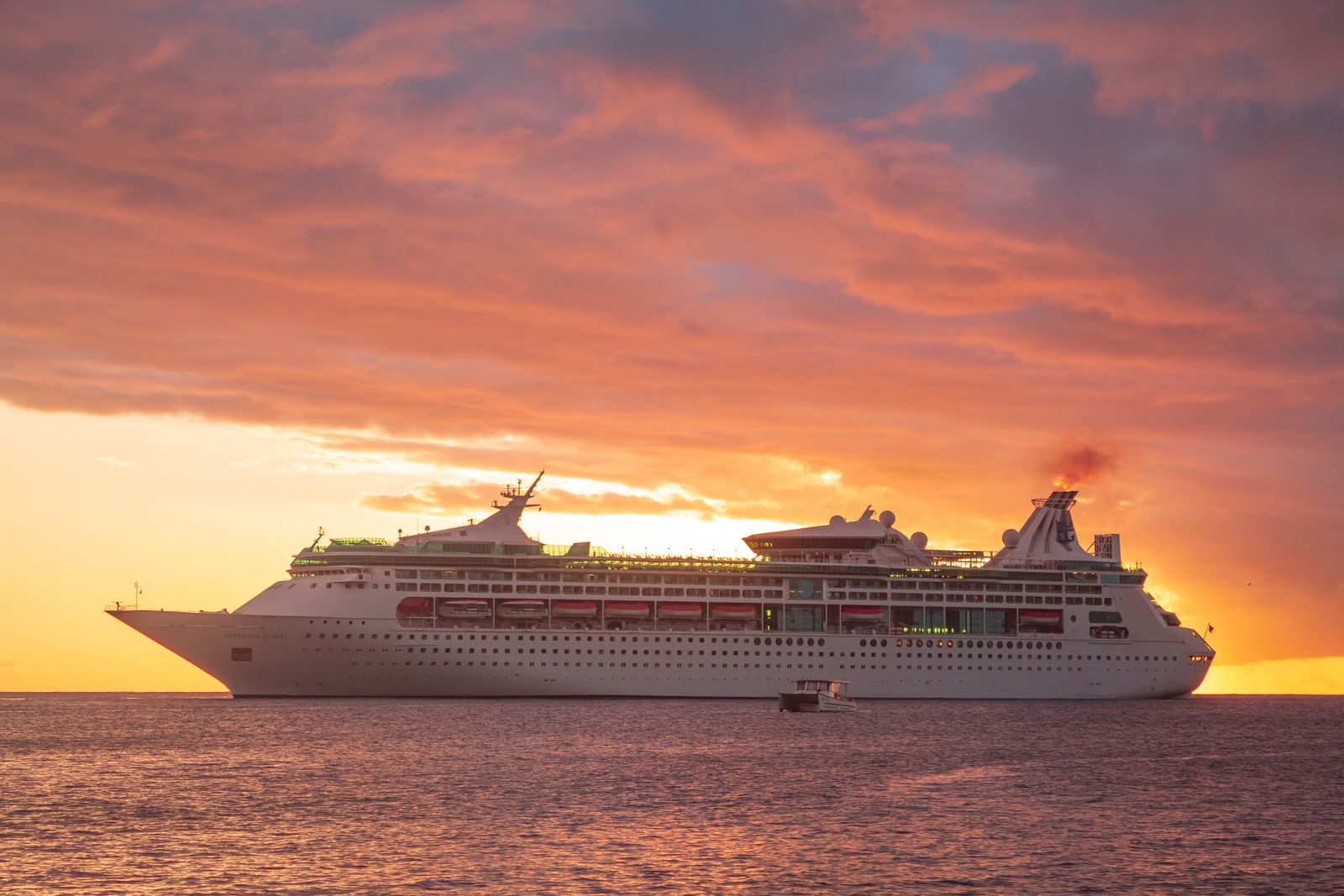 A cruise ship sailing across a calm sea under a fiery orange sunset, the kind of evening adults look for in the best cruise line for adults