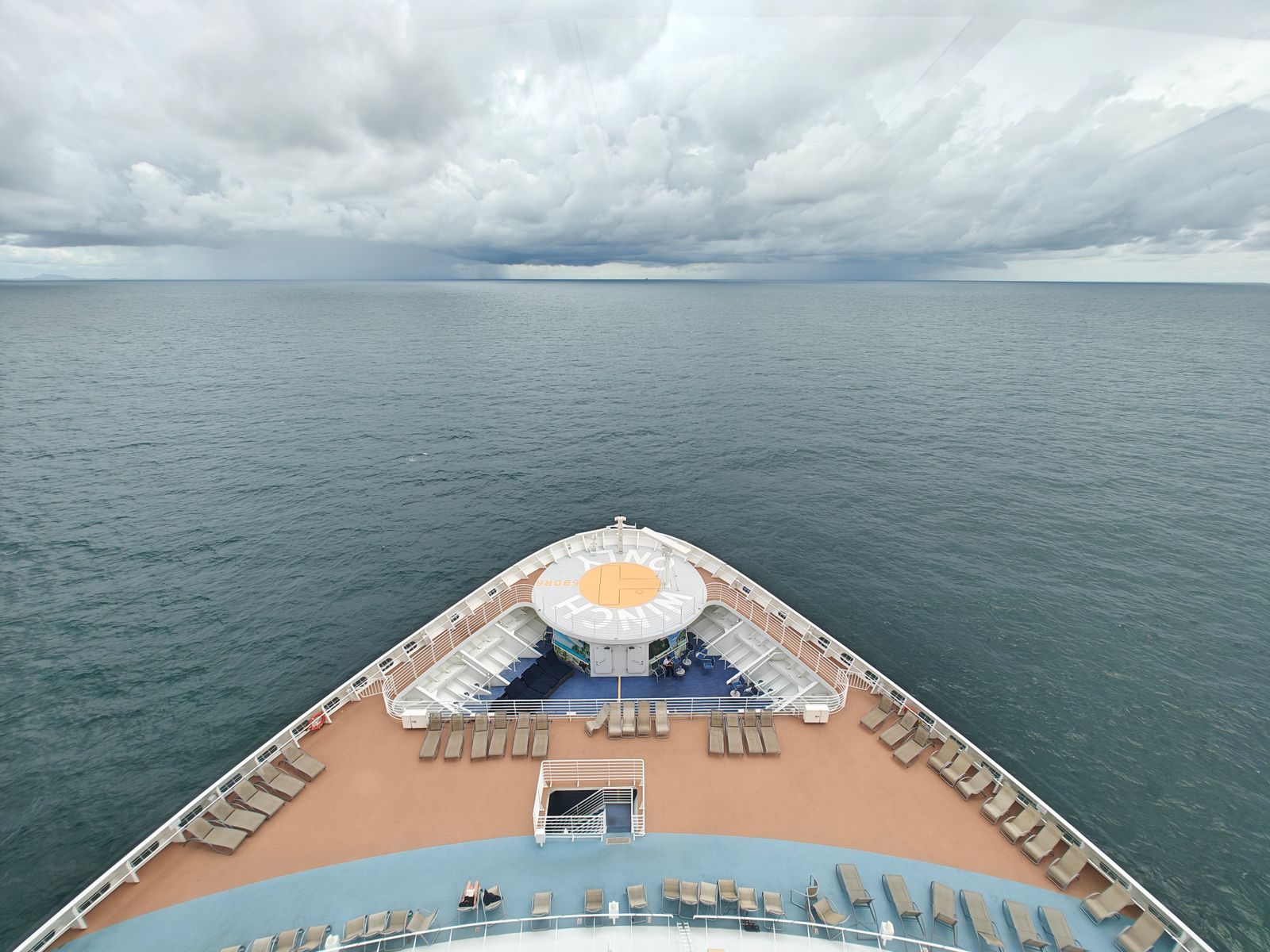 The bow of a cruise ship heading out across a calm grey sea under heavy clouds, the starting point for deciding which cruise line is best