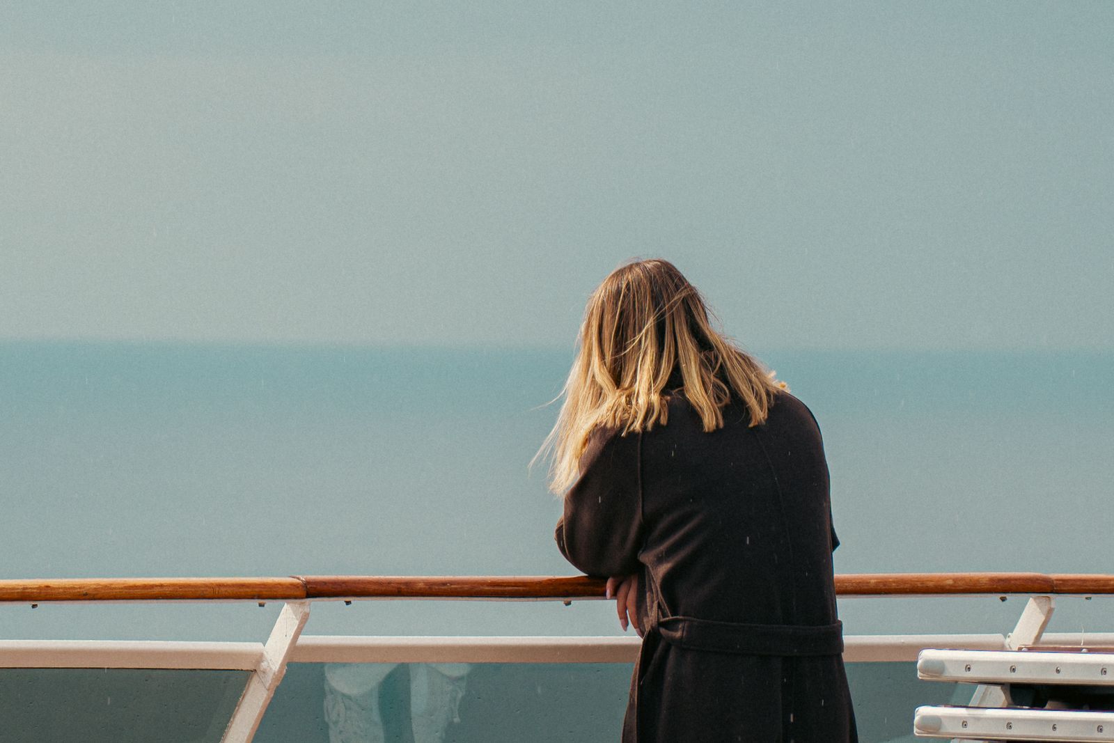 A woman traveling alone leaning on a ship&rsquo;s rail and looking out over a misty sea, a common scene for solo travelers at sea